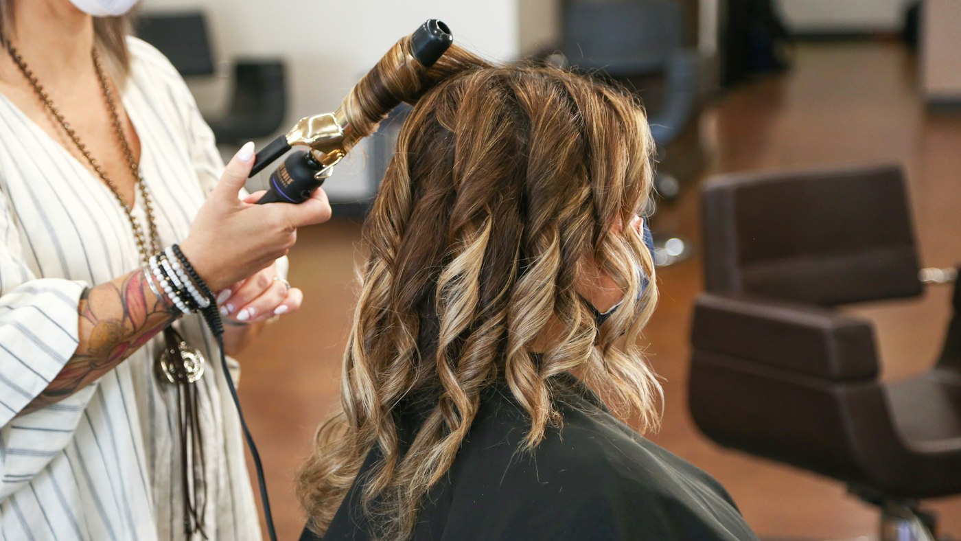 A hairstylist curling a client's hair in a salon