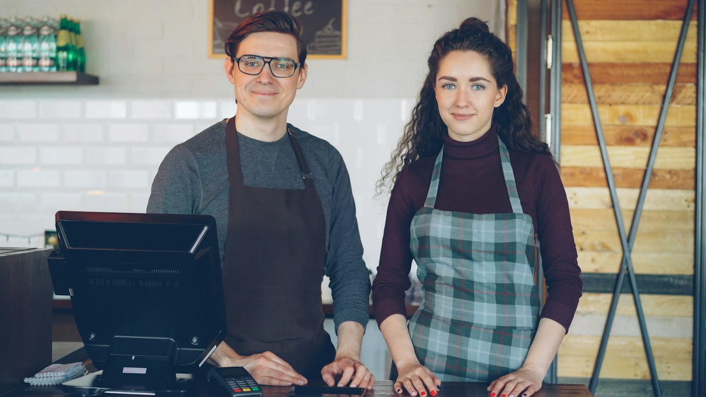 Two baristas ready for service behind their coffee shop counter