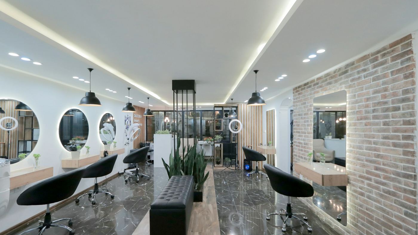 The interior of a modern hair salon, with styling chairs and round mirrors along an exposed brick wall