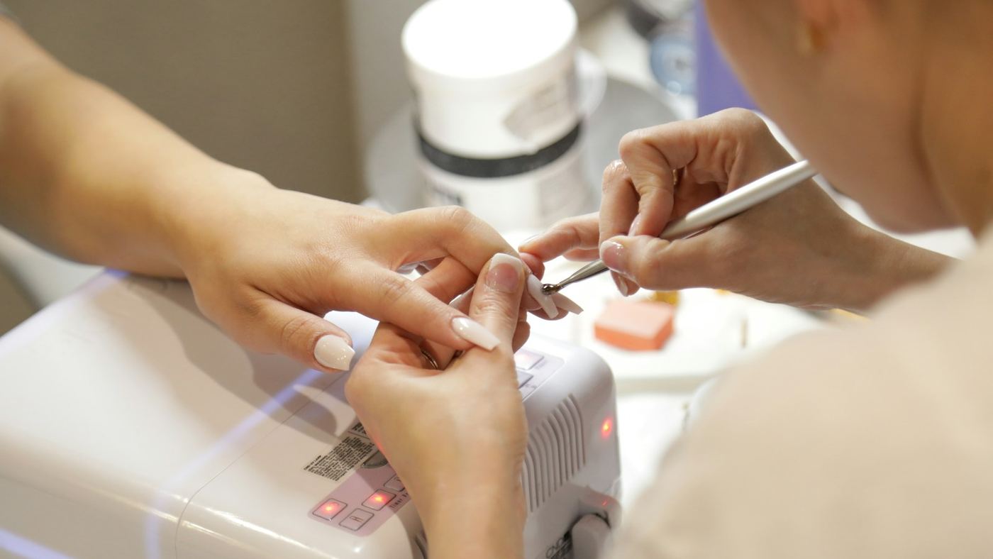 A nail technician shaping a client’s nails under a manicure lamp